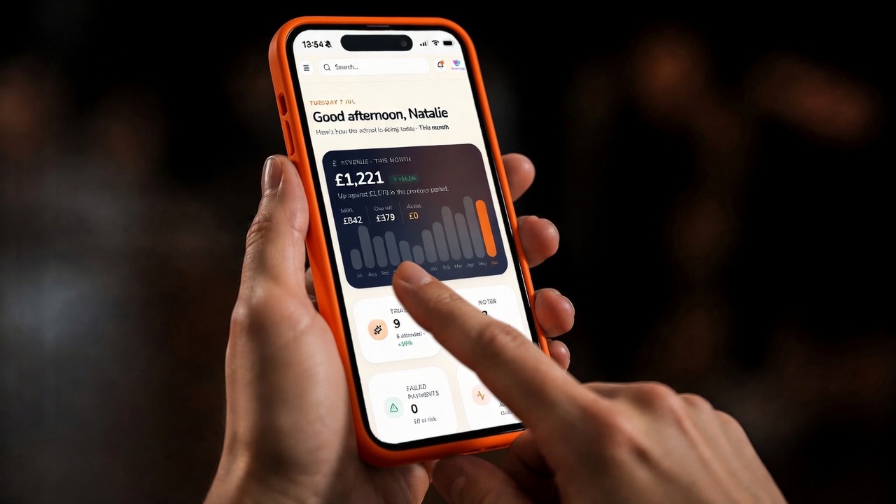 Studio owner holding a phone showing the Enrolio revenue dashboard for the month.