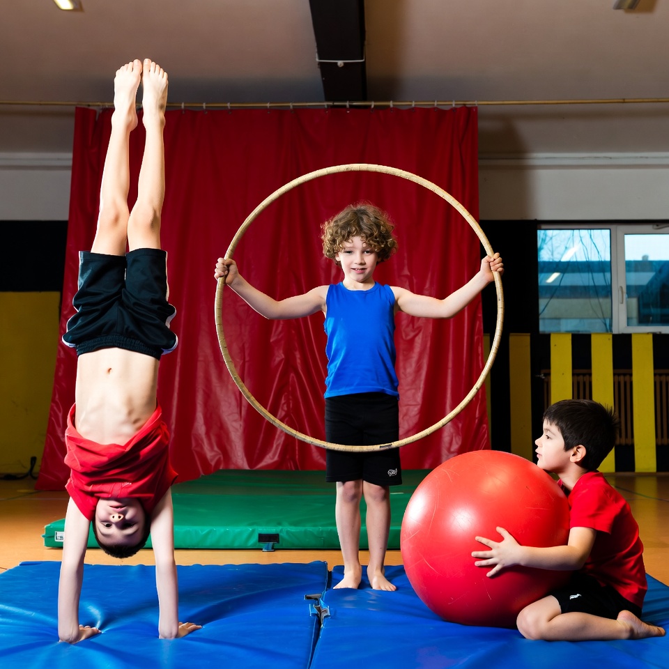 Aerial silks performer mid-air against deep red theatre curtains.